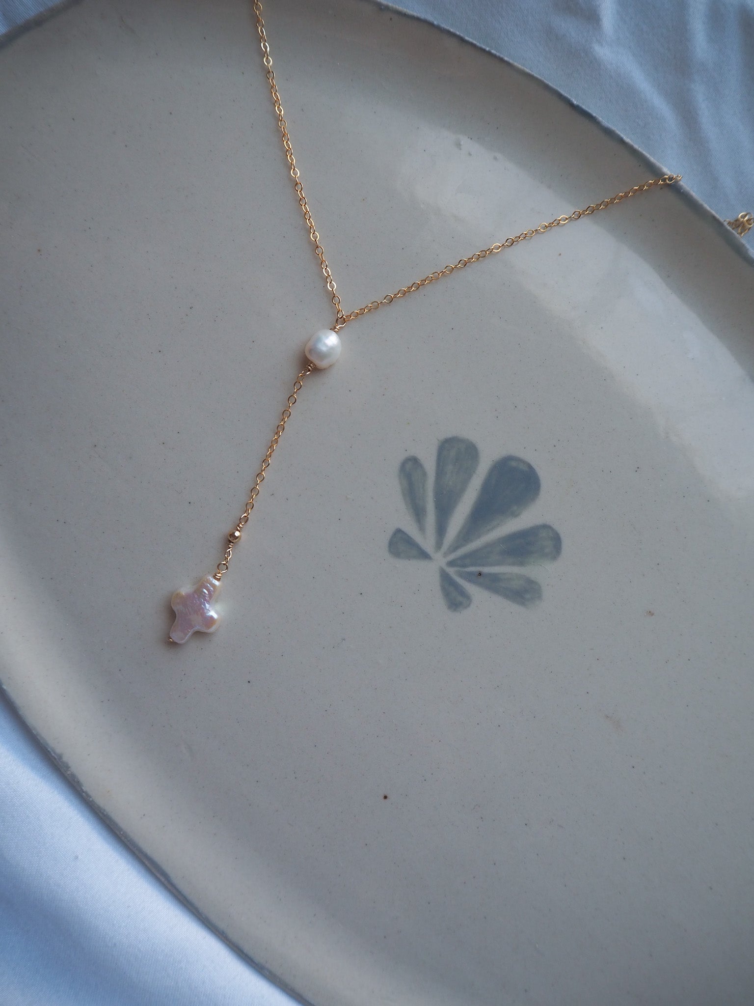 Minimal gold lariat pearl cross necklace flat lay with freshwater pearl and cross drop pendant, handmade coastal jewelry necklace