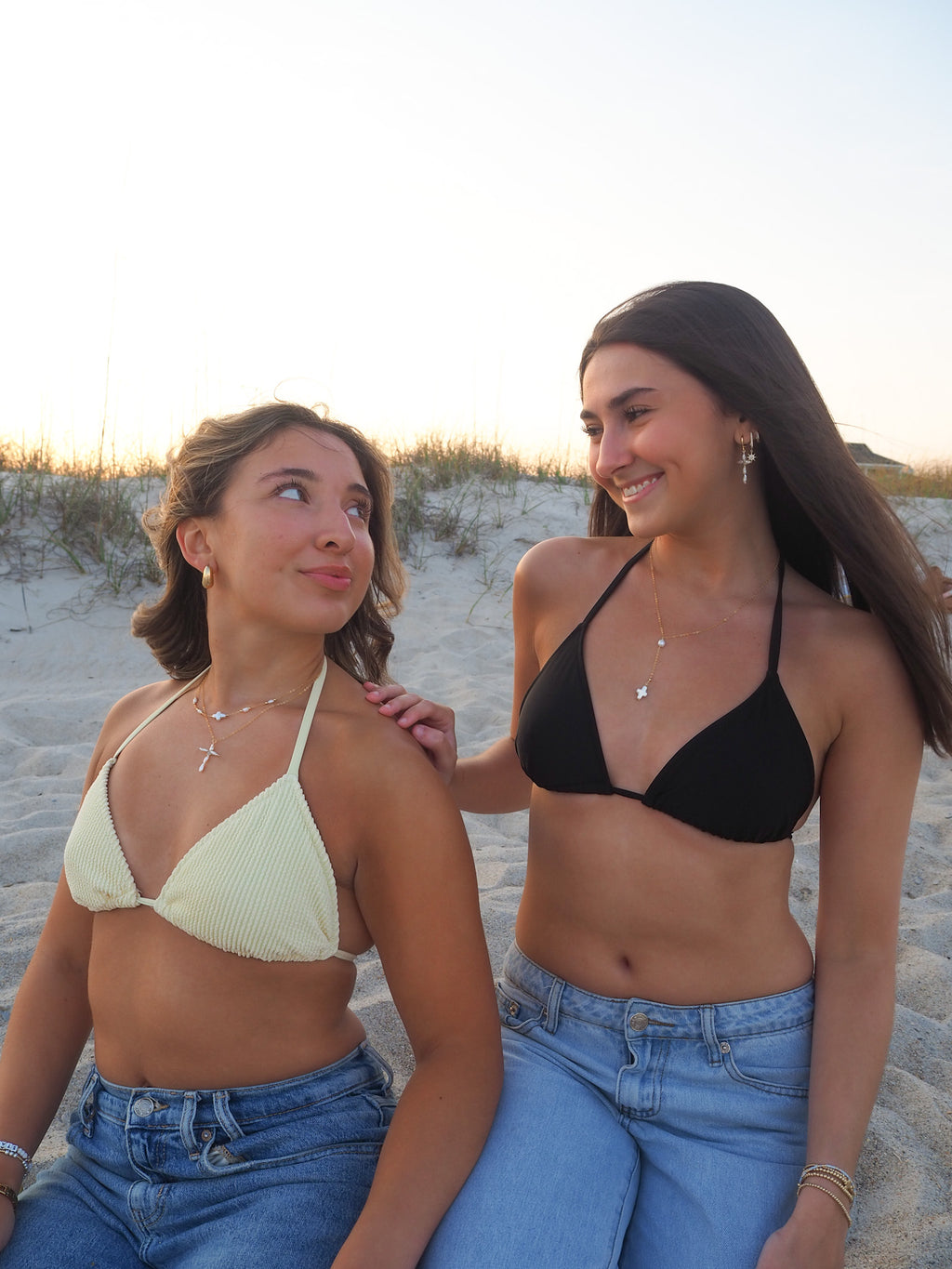 Women wearing layered pearl cross necklace and gold necklace on the beach, handmade coastal jewelry styled for summer