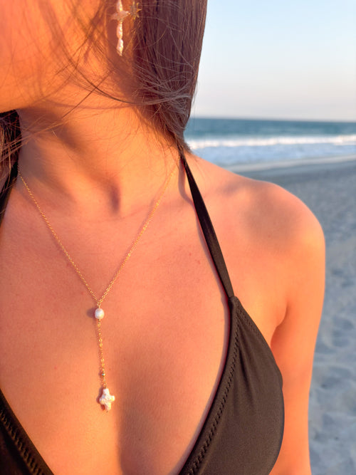Gold lariat pearl cross necklace worn at the beach, featuring a freshwater pearl drop and cross pendant on a delicate chain