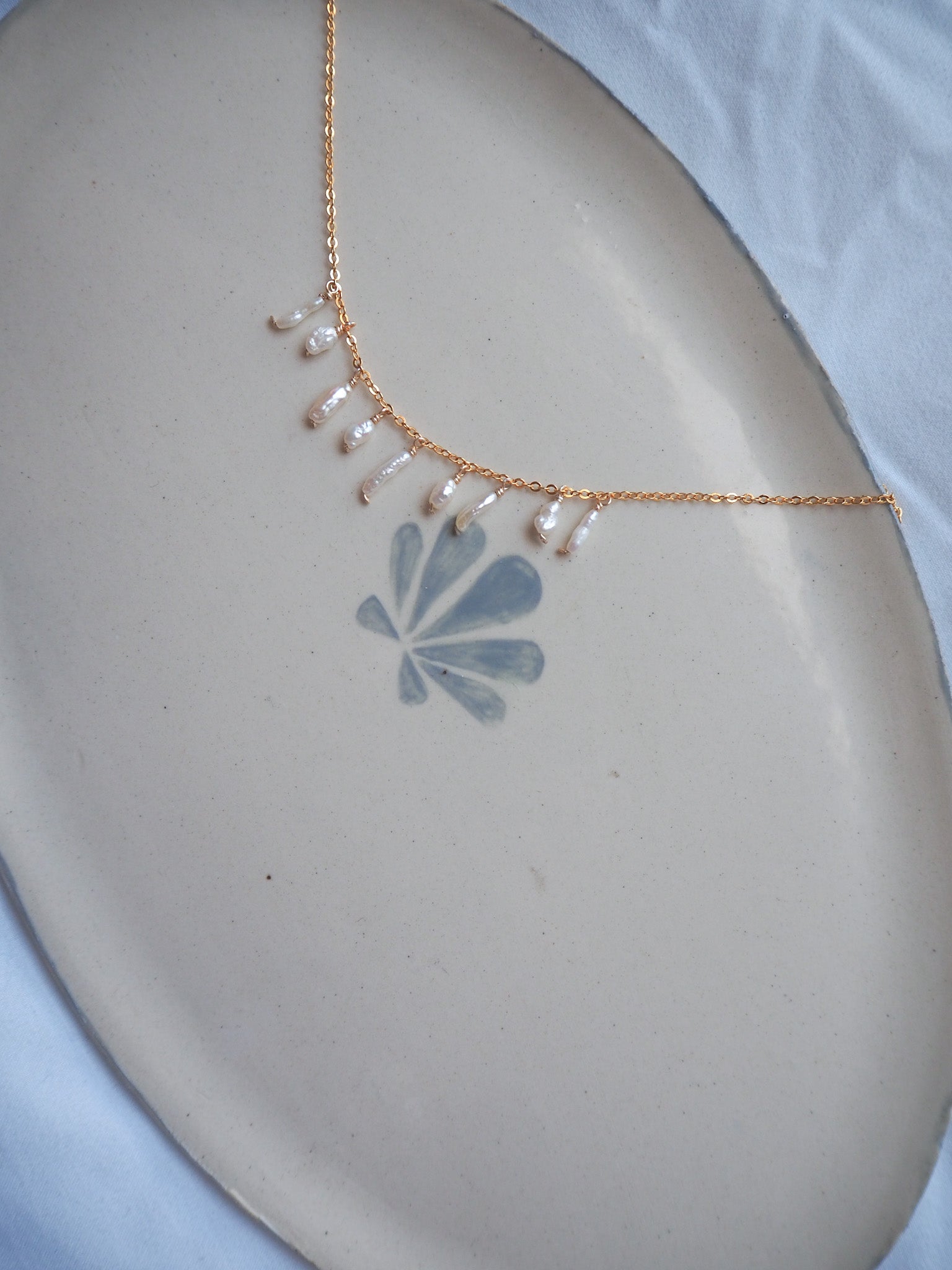 Flat lay of gold pearl drop necklace with dangling freshwater pearls on a delicate chain, minimalist coastal jewelry necklace