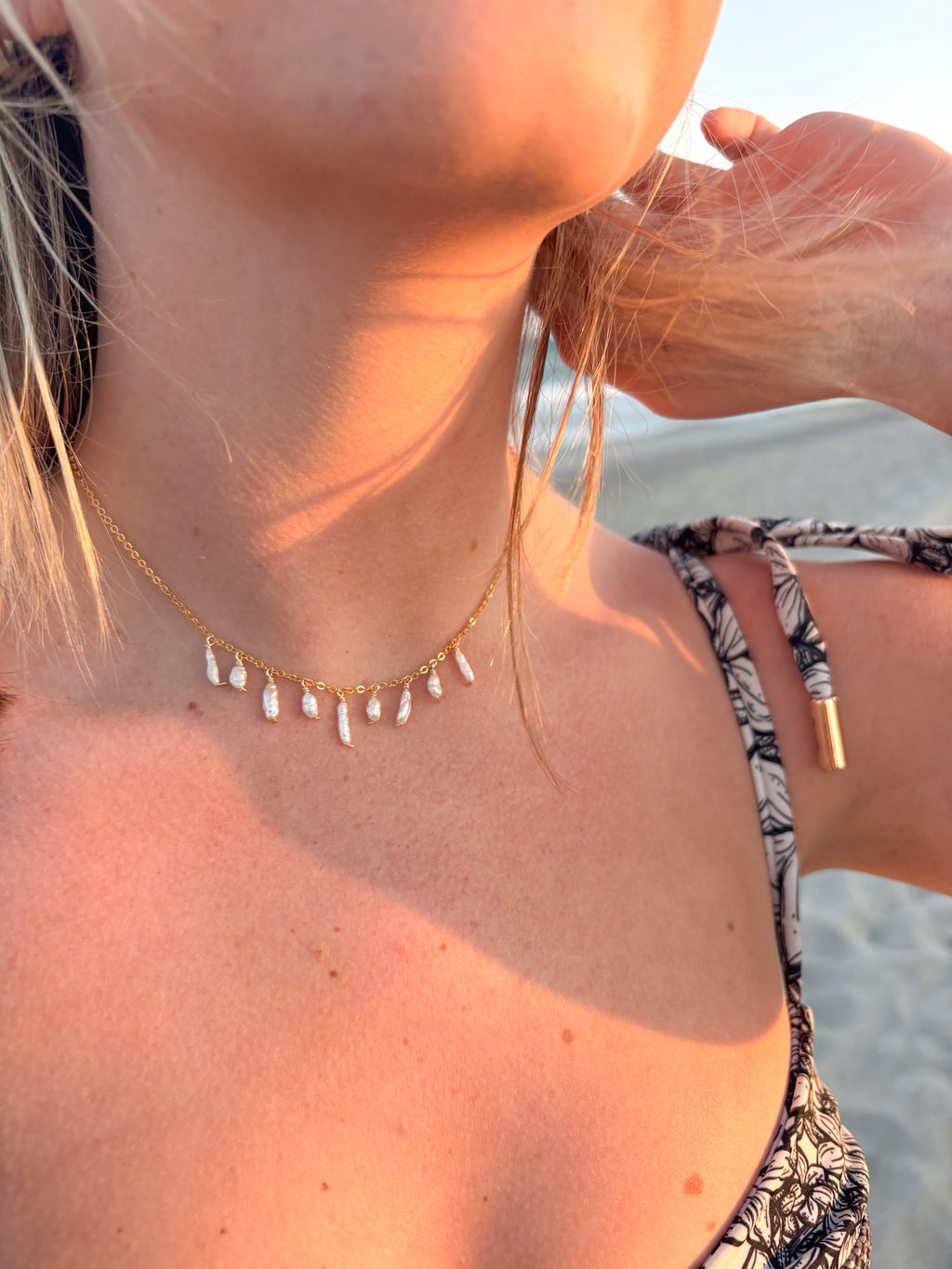 Gold freshwater pearl drop necklace worn on the beach, featuring dainty dangling pearls on a delicate chain necklace