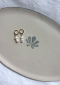 White pearl gold earrings on plate flatlay