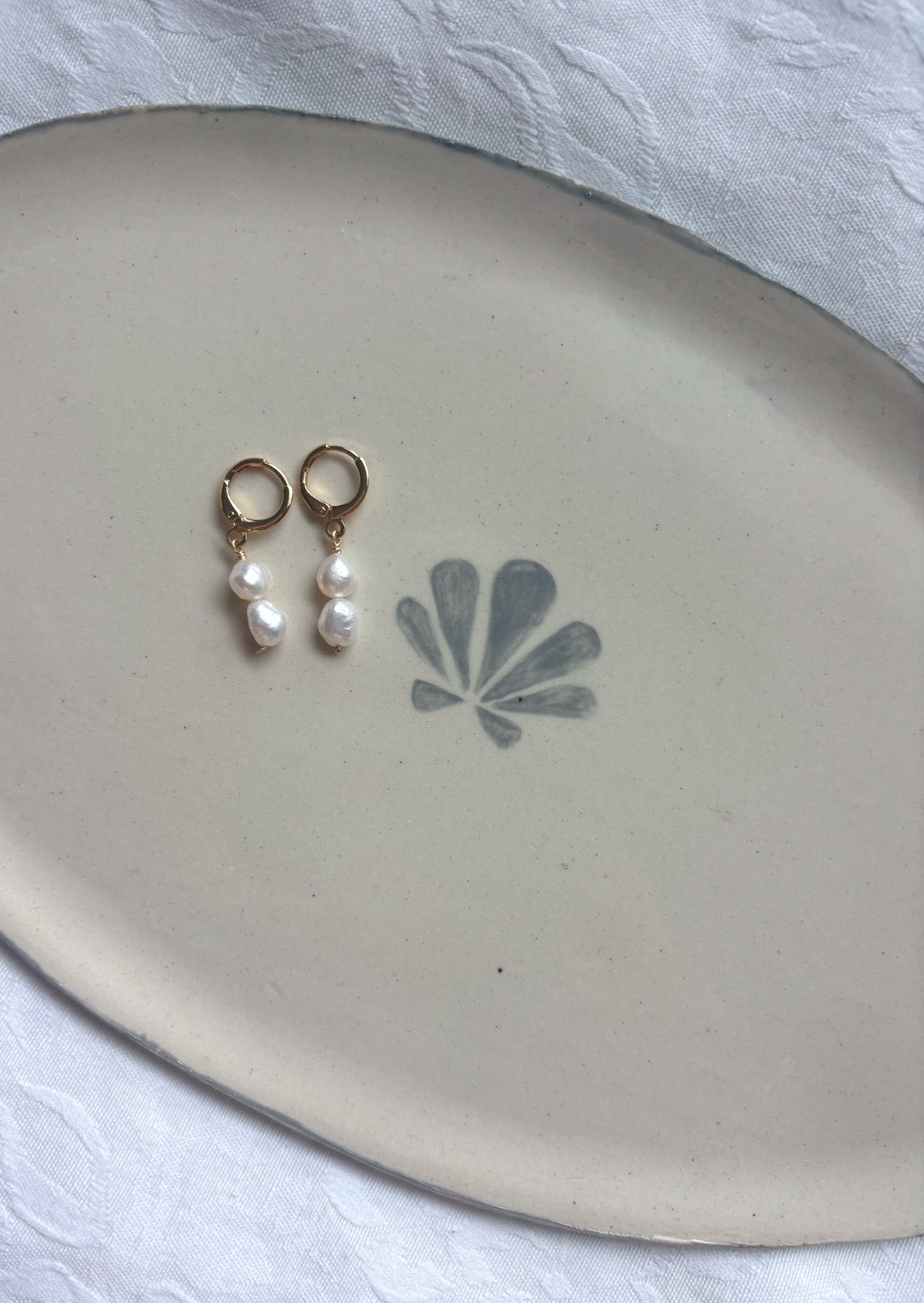 White pearl gold earrings on plate flatlay