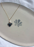 Gold necklace with pearl and shark tooth pendant on plate flat lay