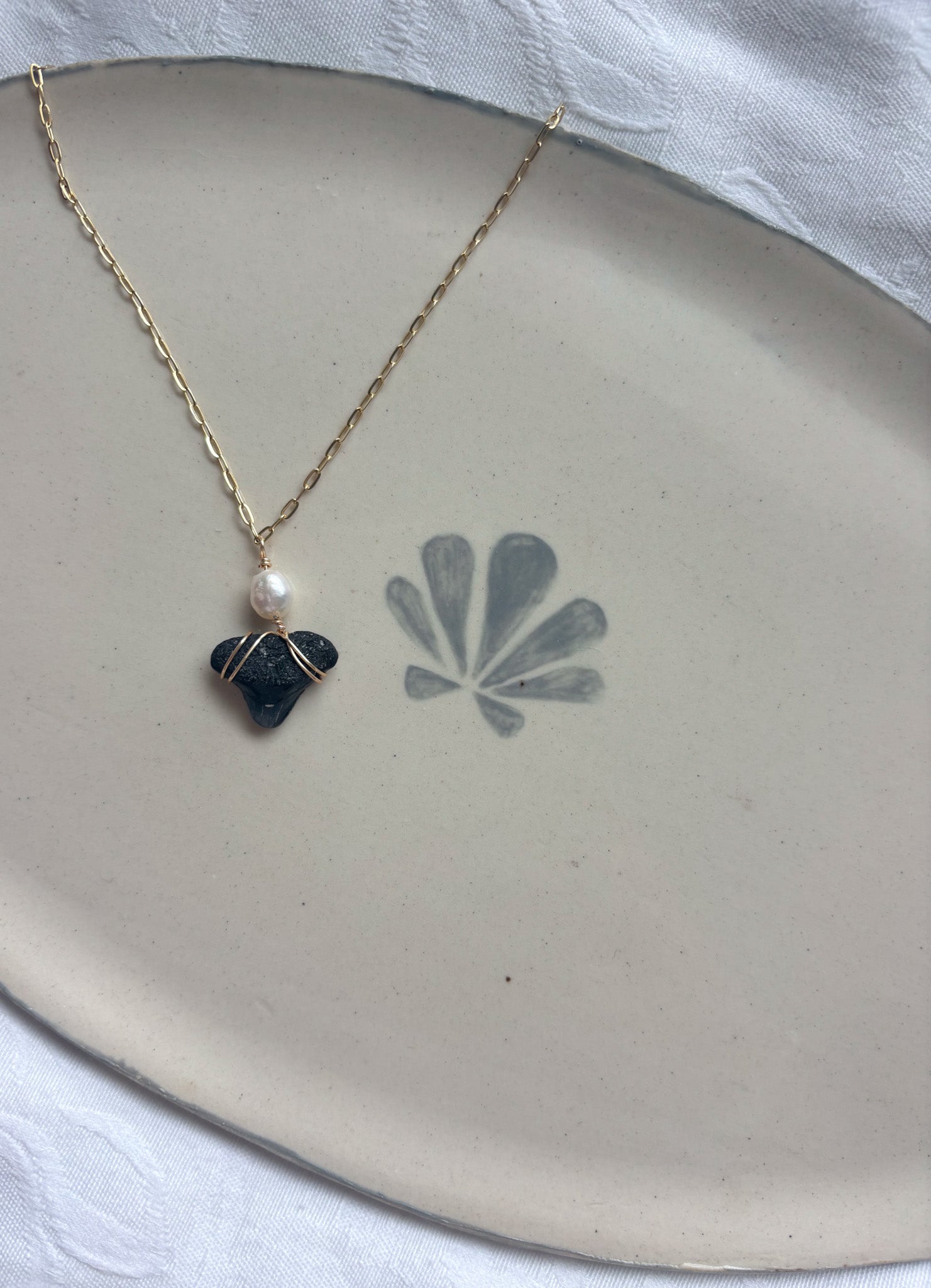Gold necklace with pearl and shark tooth pendant on plate flat lay