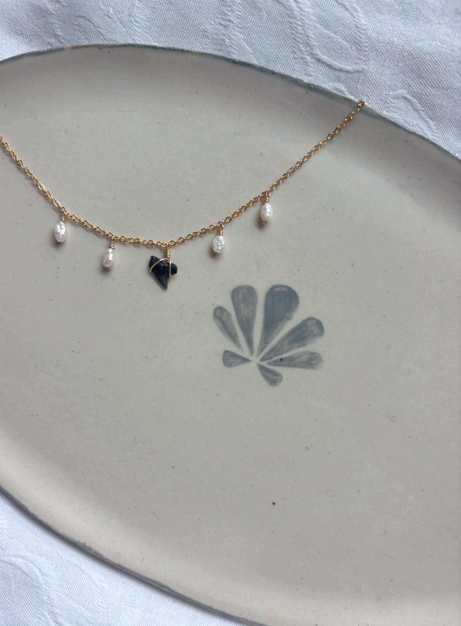 Gold shark tooth and pearl charm necklace on dainty chain flat lay photo