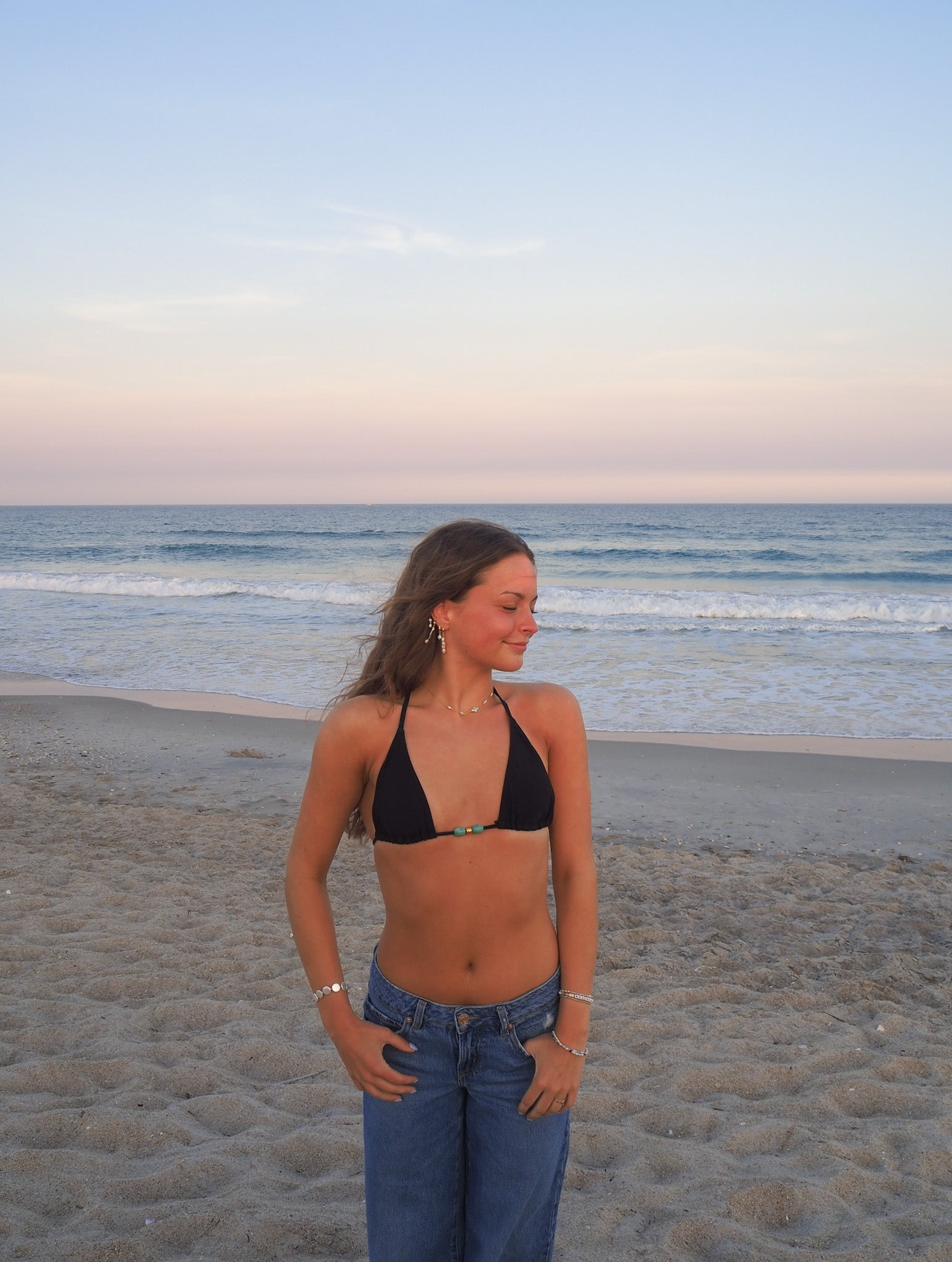 Handmade pearl cross necklace worn on beach with casual denim outfit, delicate gold chain coastal jewelry for everyday layering