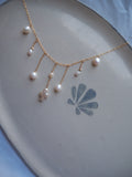 Dainty pearl cross necklace flat lay with freshwater pearl drops on gold chain, handmade coastal beach jewelry necklace design.