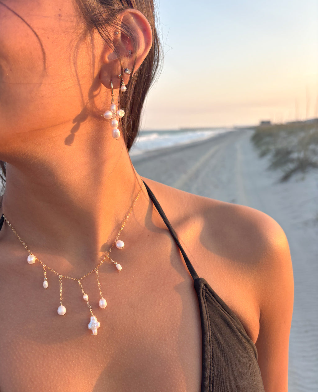 Dainty pearl cross necklace with freshwater pearl accents on gold chain worn at beach, handmade coastal jewelry with matching pearl earrings.